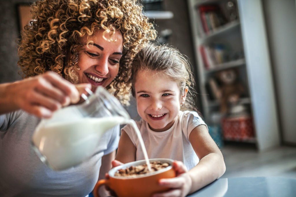 Portrait of adorable young girl and mother having breakfast